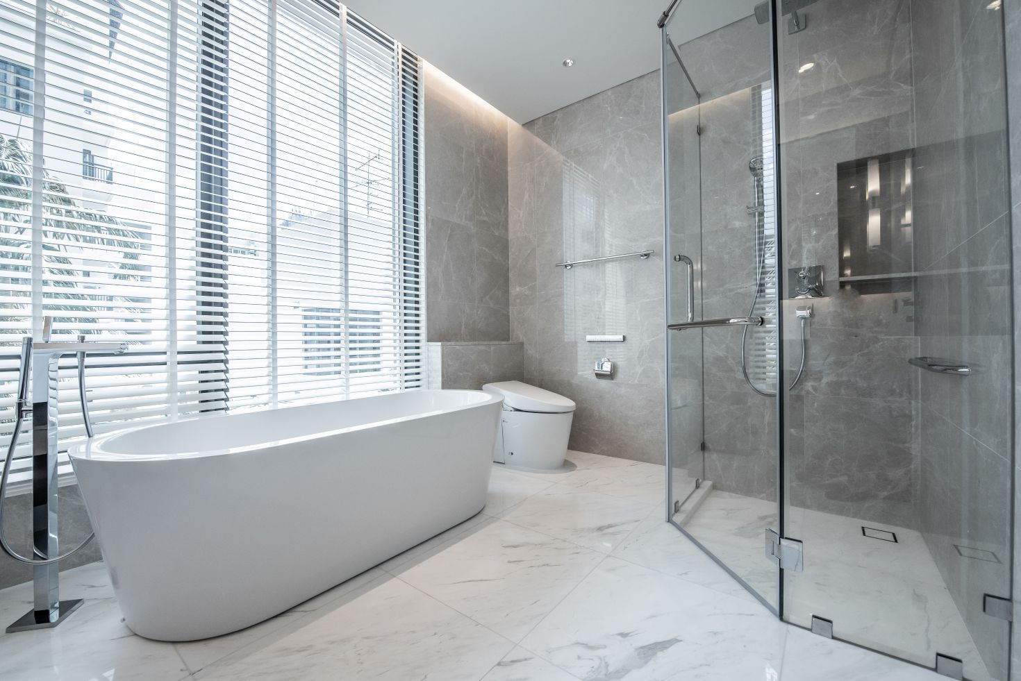 A modern bathroom featuring a white freestanding bathtub, a glass-enclosed shower, and a toilet against marble-tiled walls.