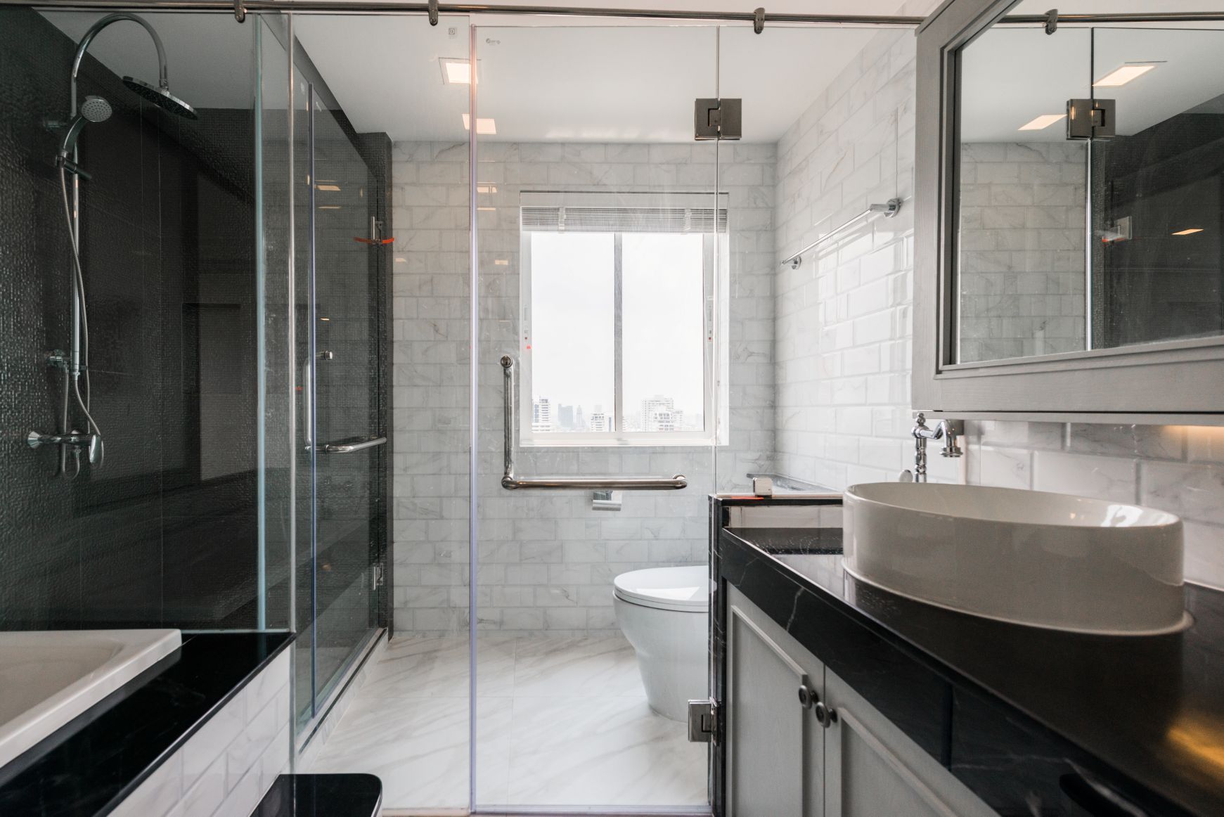 Modern bathroom featuring a black vanity with a white vessel sink, a walk-in glass shower, and a white toilet by a window.