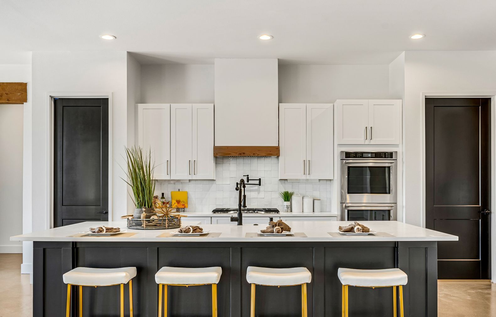 Modern kitchen with white cabinets, a dark gray island with four stools, stainless steel appliances, and two dark doors.