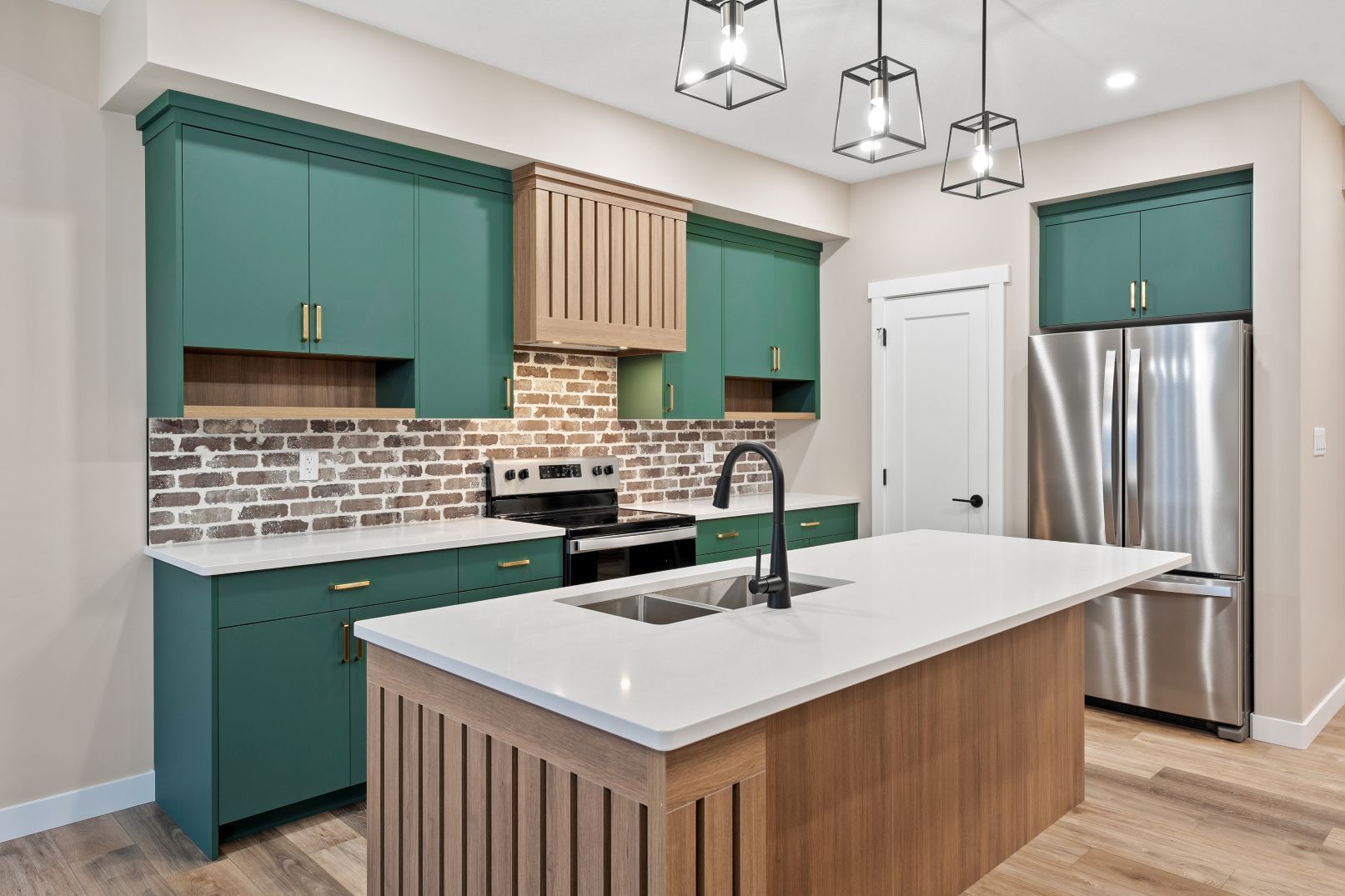 A kitchen with teal cabinets, wood-tone island and vent hood, white countertops, a brick backsplash, and stainless fridge.