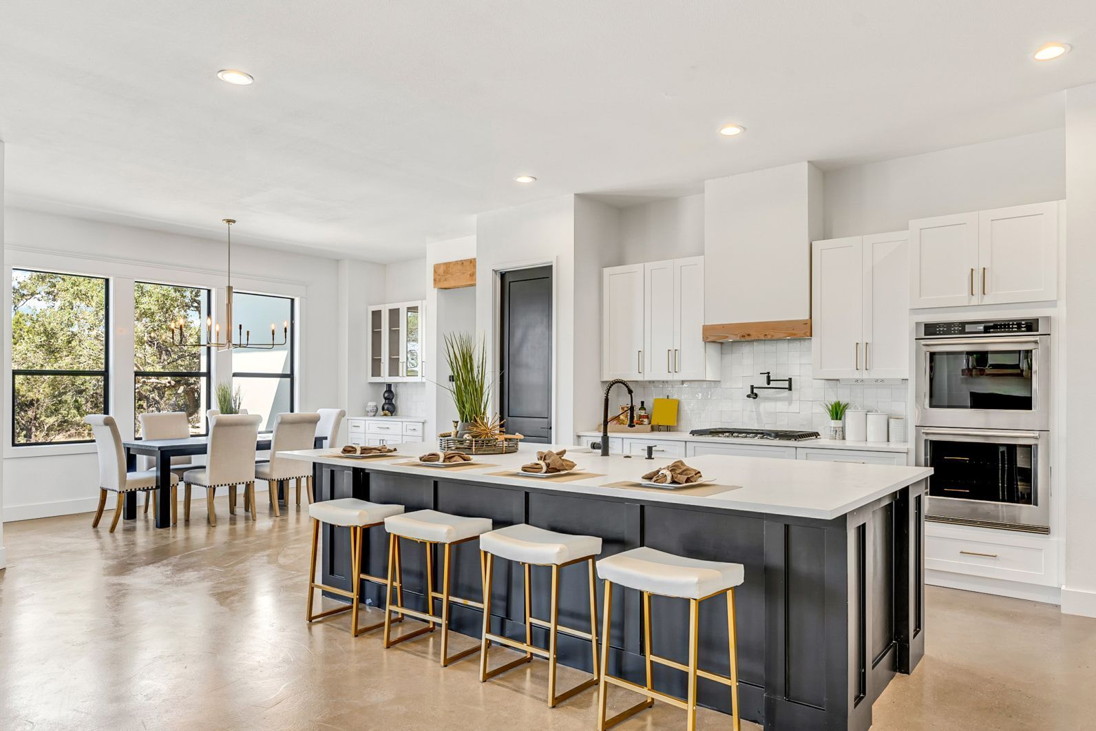 A modern open-plan kitchen featuring a dark blue island with white stools, white cabinetry, and a dining area.