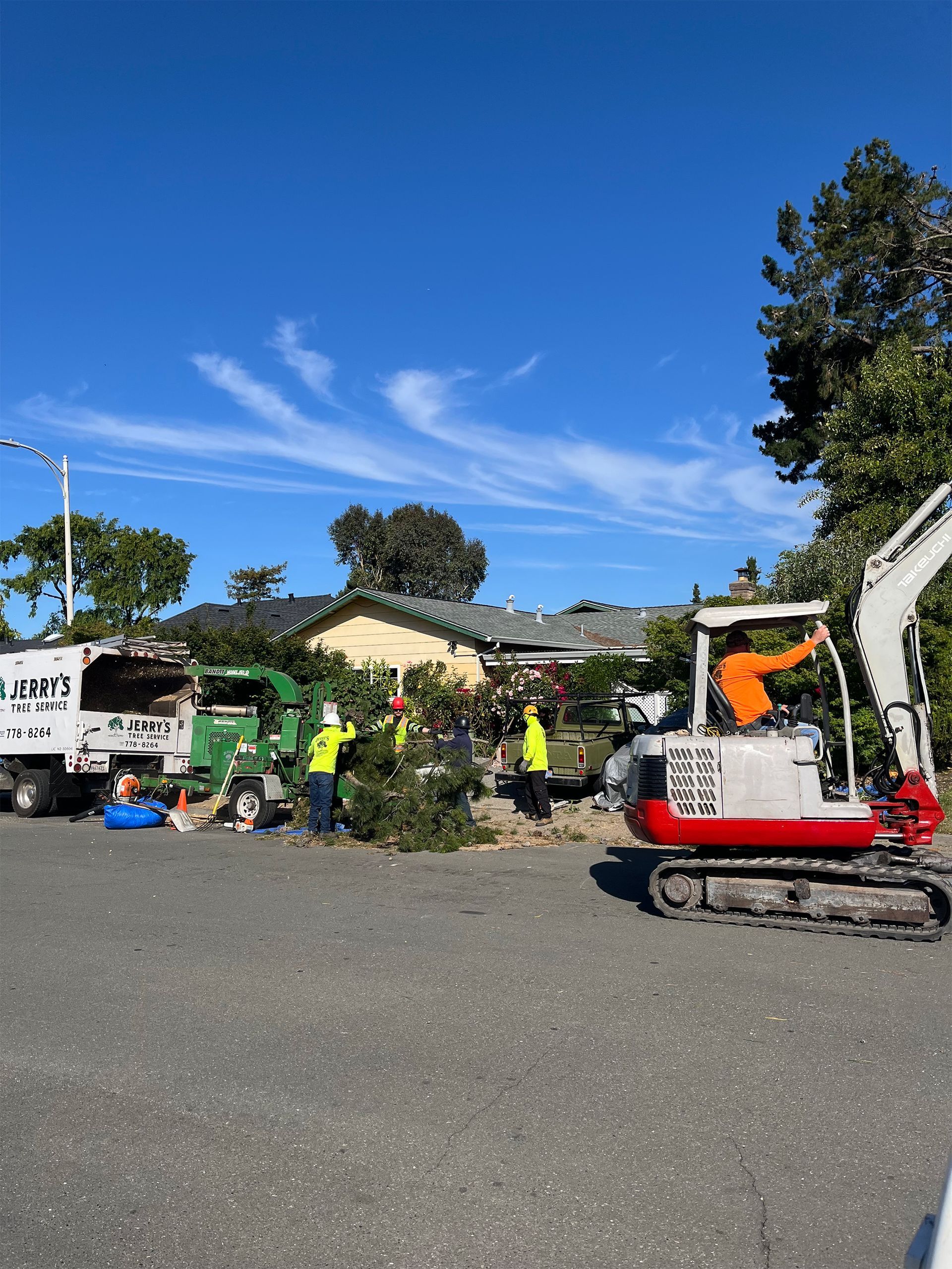 Construction workers with a mini excavator clearing debris beside a green truck under a bright blue sky