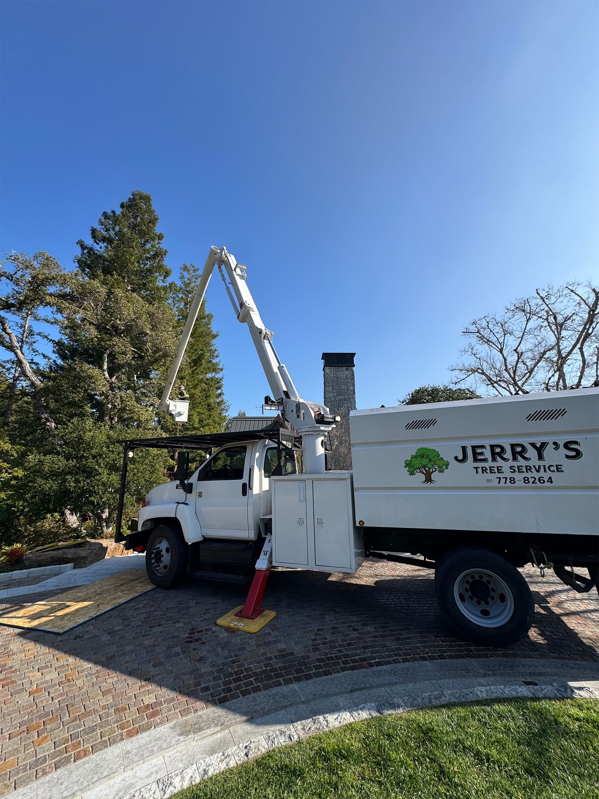White utility truck with crane and Jerry’s logo parked on a gravel driveway under a blue sky
