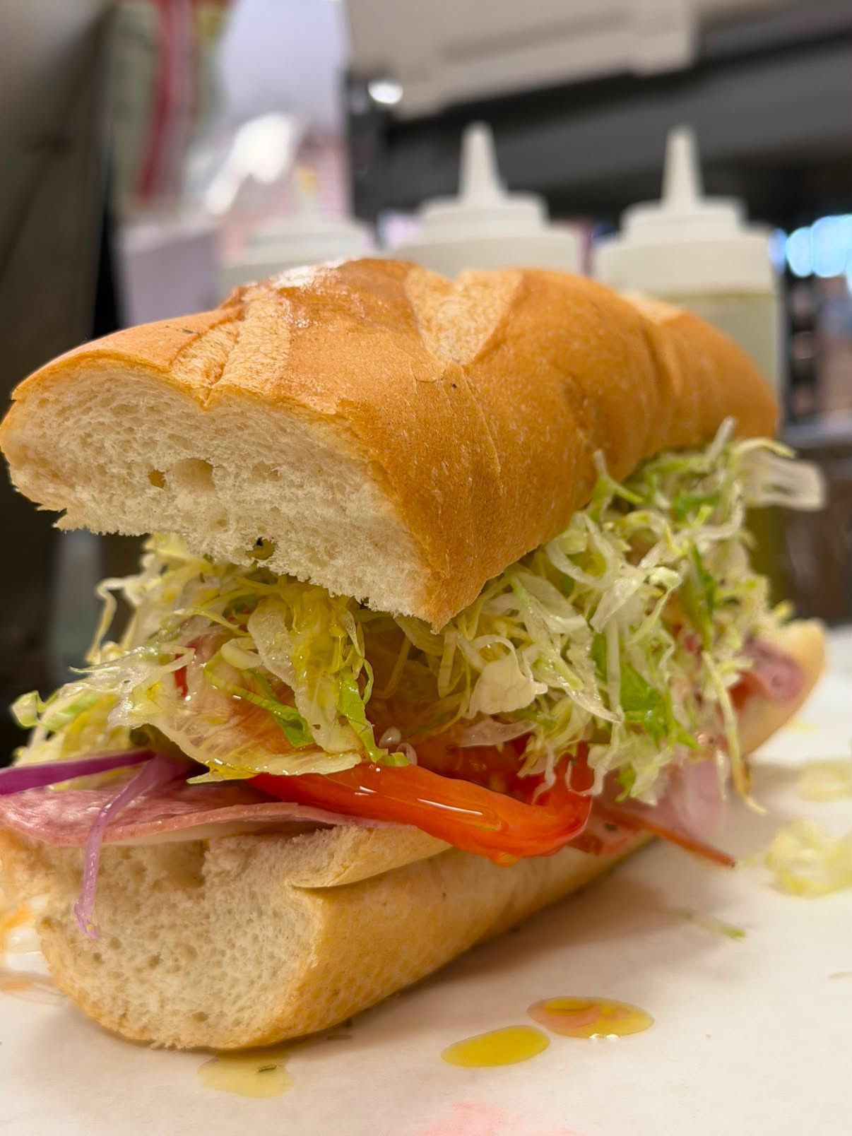 Sub sandwich with lettuce, tomato, and red onion on a white plate in a kitchen setting.