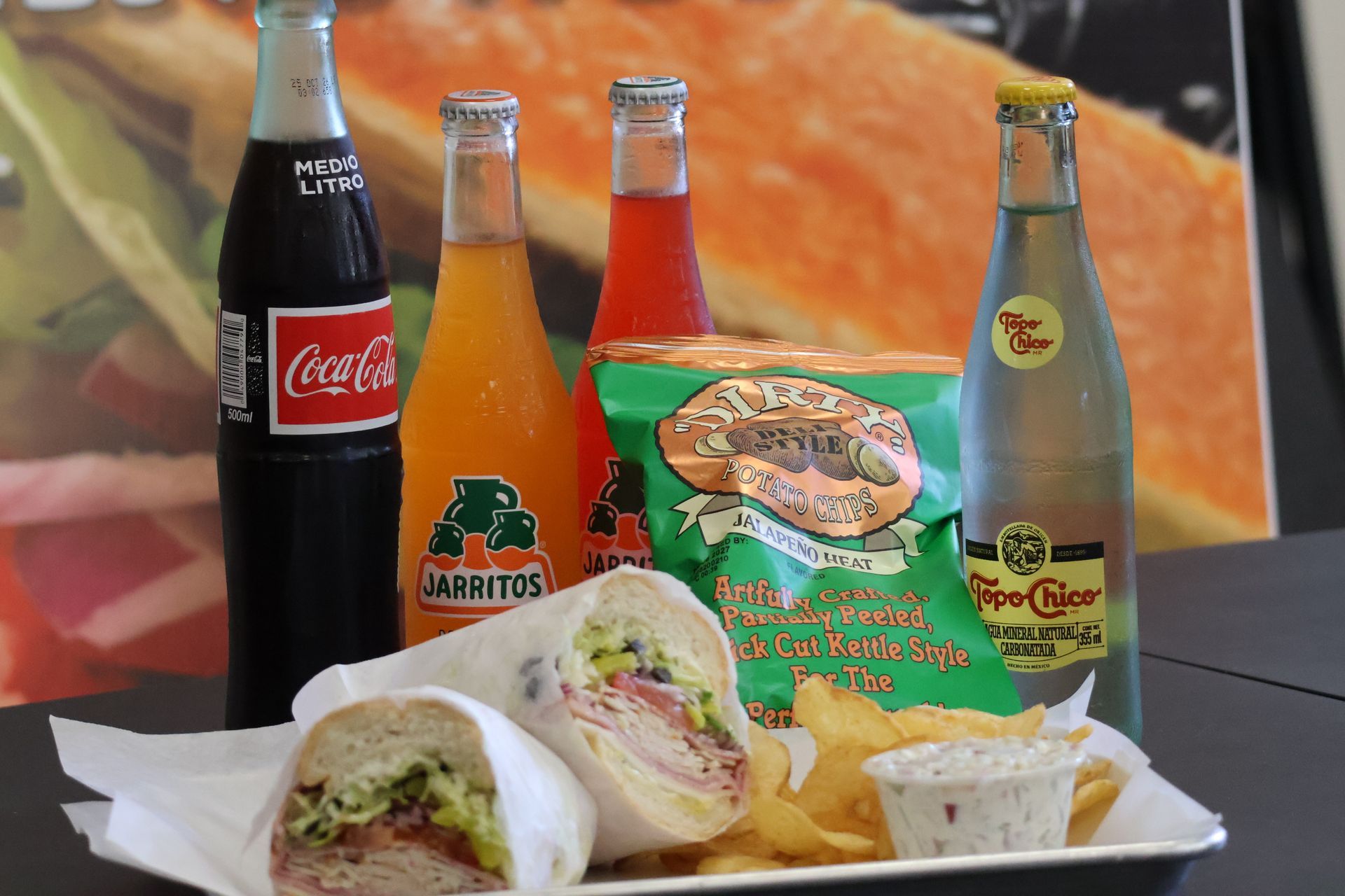 Mexican food with two burritos, chips, dip, and glass soda bottles on a table.