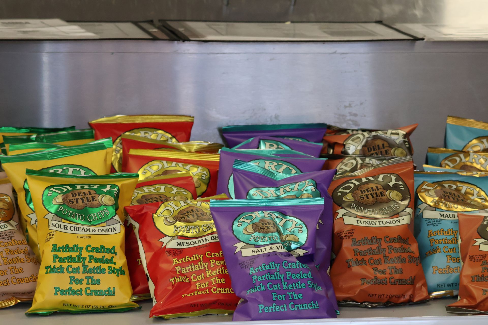 Assorted colorful snack bags arranged on a metal shelf in a store or kitchen.