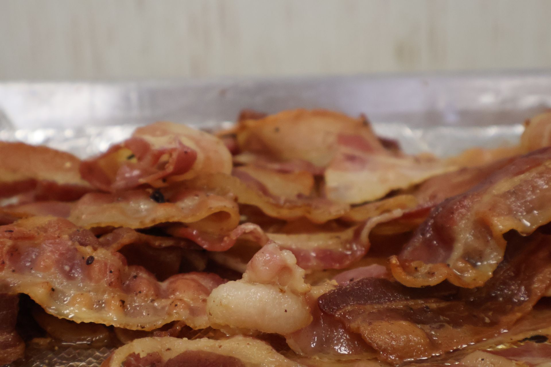 Tray of crispy cooked bacon strips on a foil-lined surface.