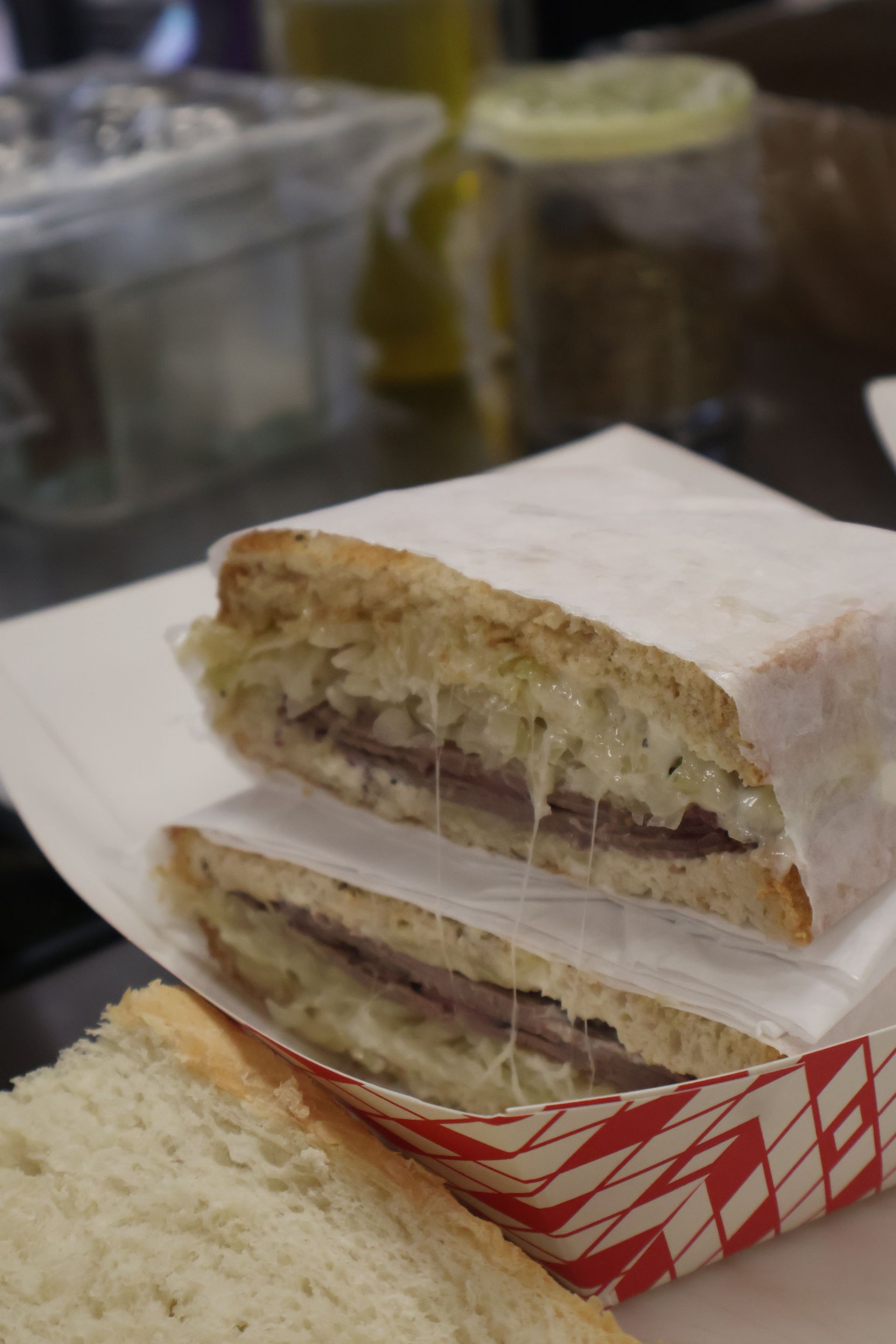Sandwich halves in white bread with meat filling on a table, with a red-and-white basket and bread slice nearby.