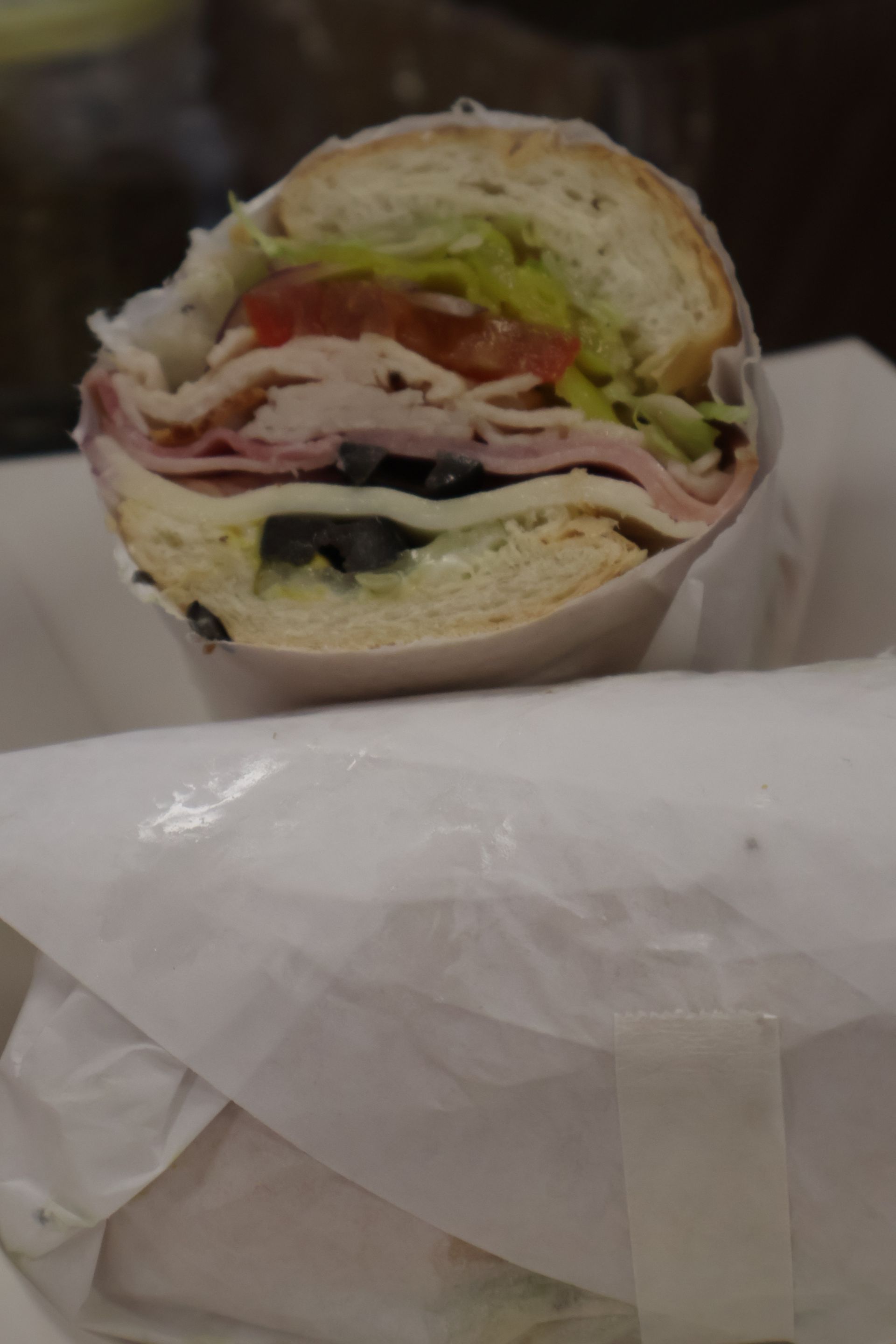 Cut sandwich with lettuce, tomato, and meat wrapped in white paper.