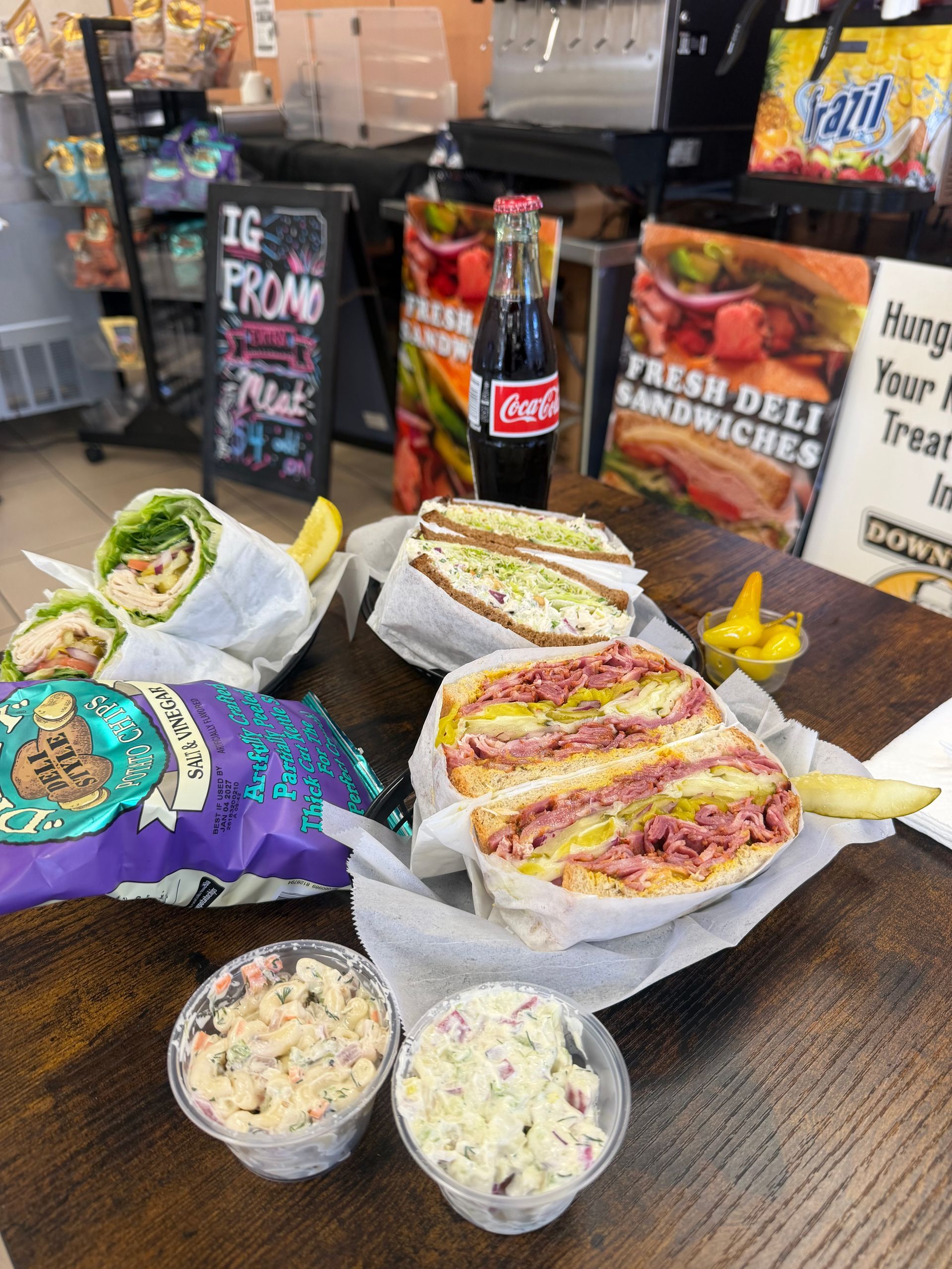 Wraps and sandwiches on a café table with two small side cups and menu signs in the background.