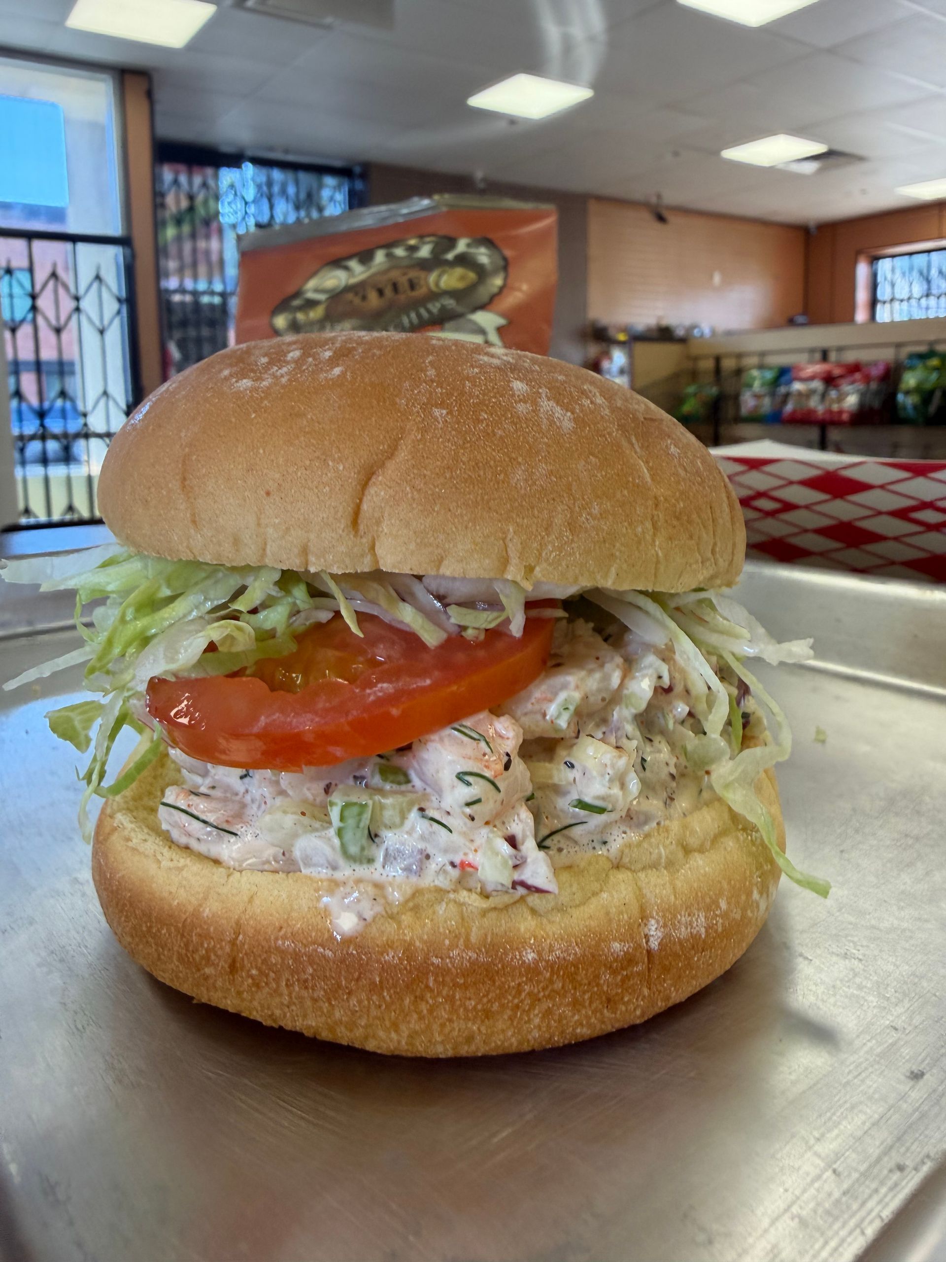 Deli sandwich with lettuce, tomato, and creamy filling on a counter in a casual restaurant.