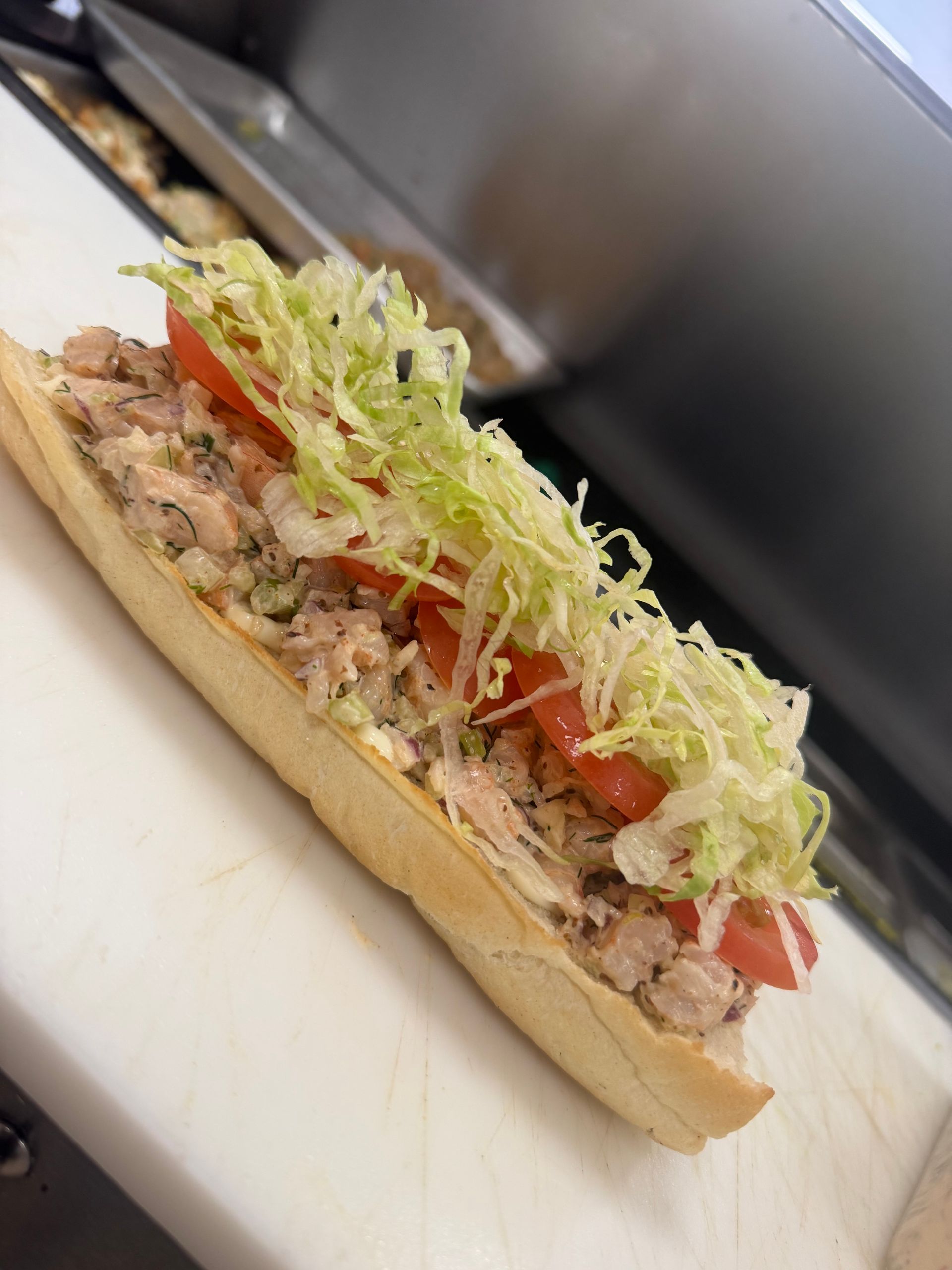 Loaded hot dog topped with shredded lettuce, diced tomatoes, and chopped meat on a bun.