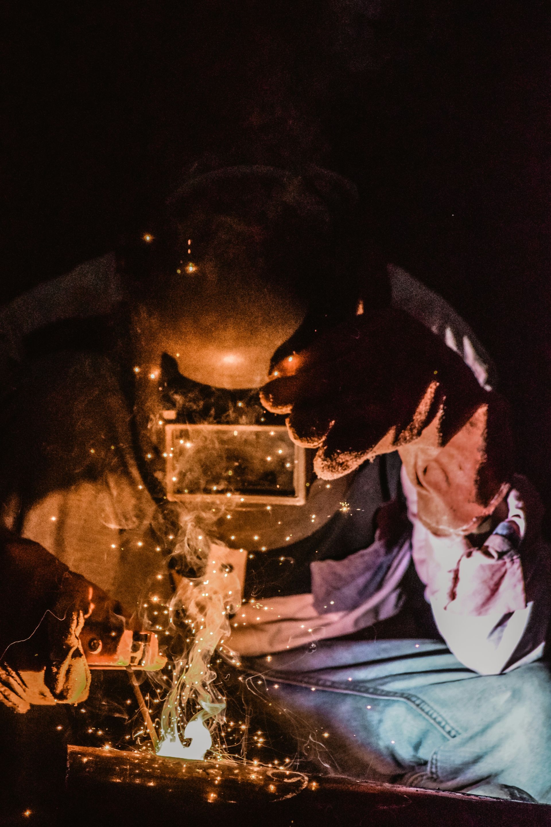 A man is welding a piece of metal in a dark room.