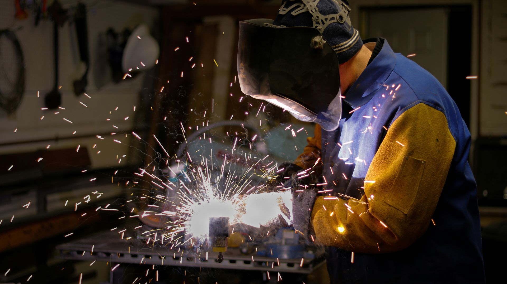 A man is welding a piece of metal in a workshop.