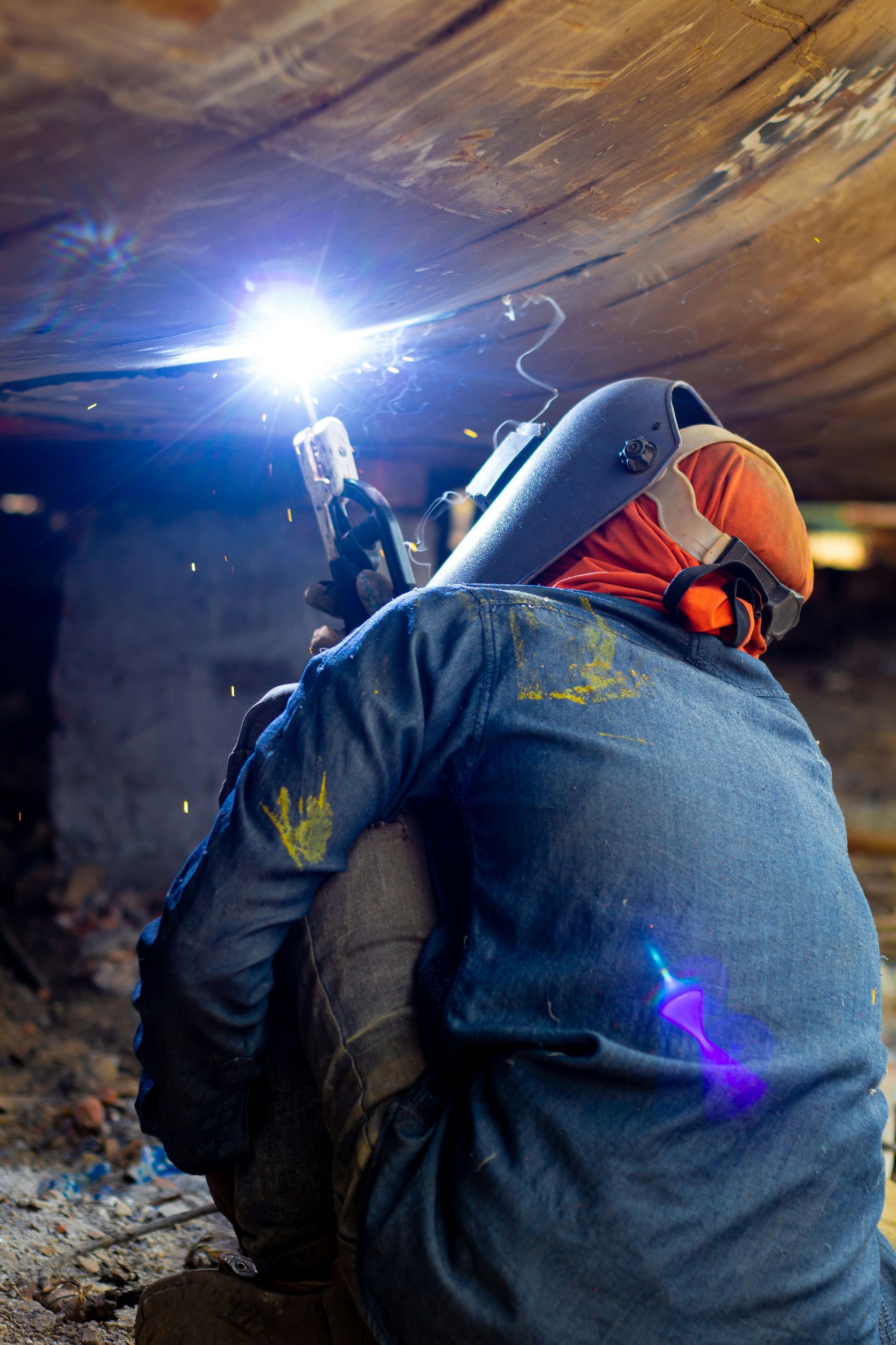 A man is welding a piece of metal in a basement.