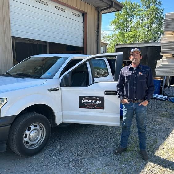 Worker standing beside a white pickup truck outside a garage on a sunny day