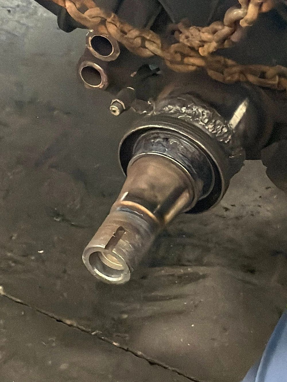 Close-up of a metal hose fitting with rust and a chain in the background on a gray surface