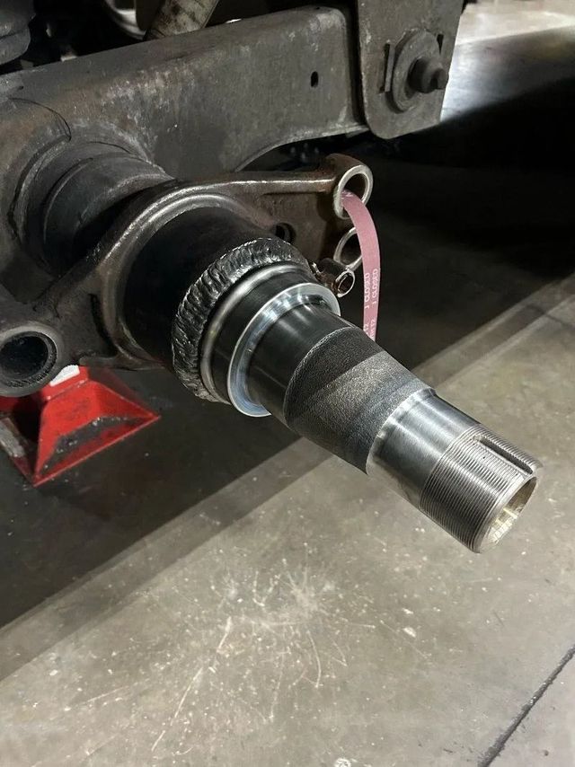 Close-up of a damaged metal shaft on industrial machinery, with grease and wear marks visible.