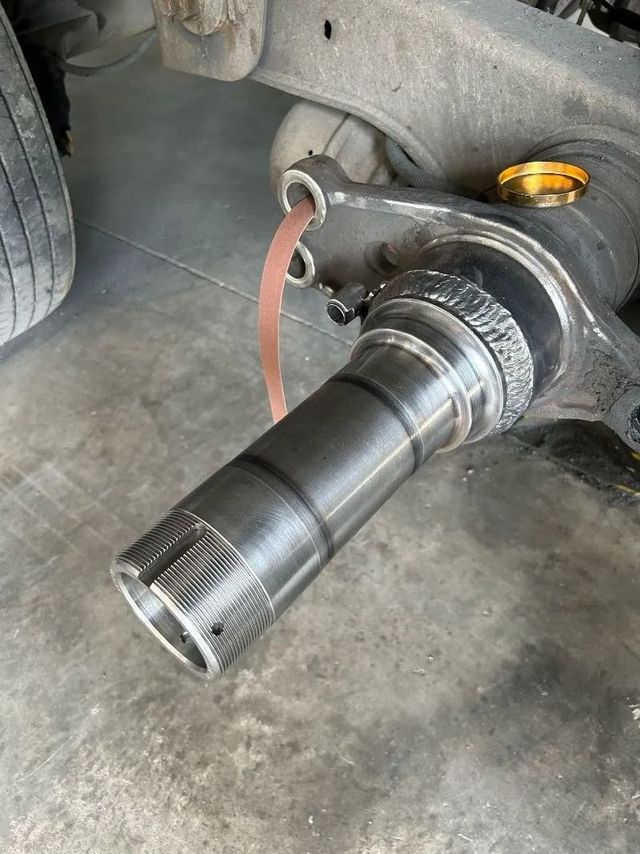 Car wheel hub and axle assembly exposed under a vehicle, with a yellow jack stand in the background