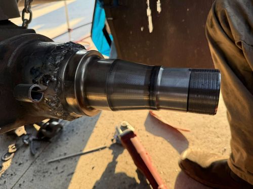 Close-up of a black metal shaft with a threaded end, attached to machinery on a worksite.