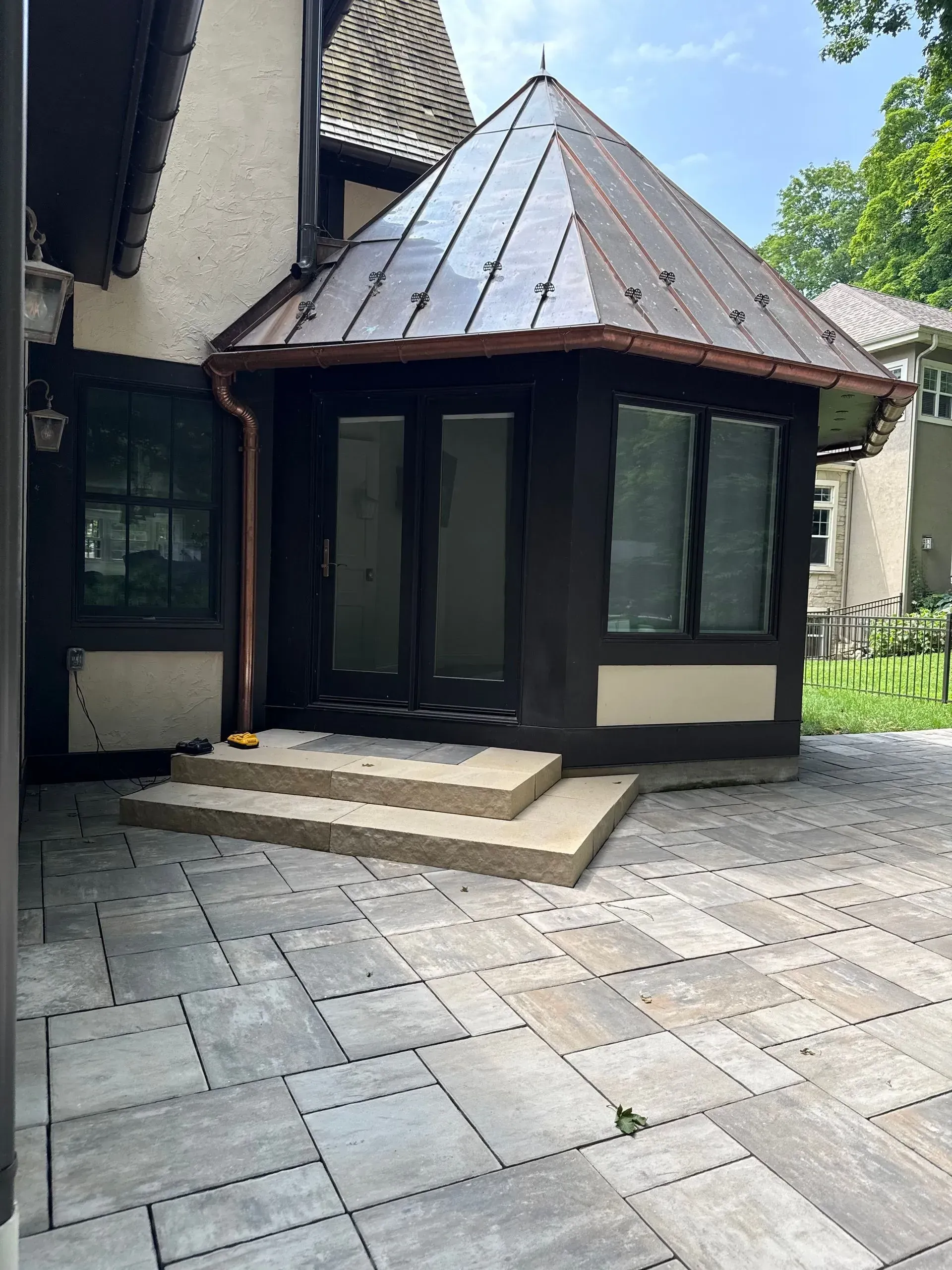 Courtyard entrance with glass doors, small steps, and a steep brown roof beside a stone patio.