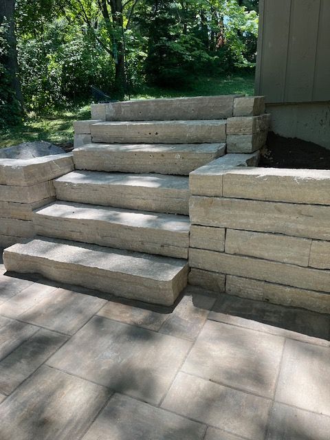 Stone steps leading up, built into retaining walls, surrounded by pavers and trees.