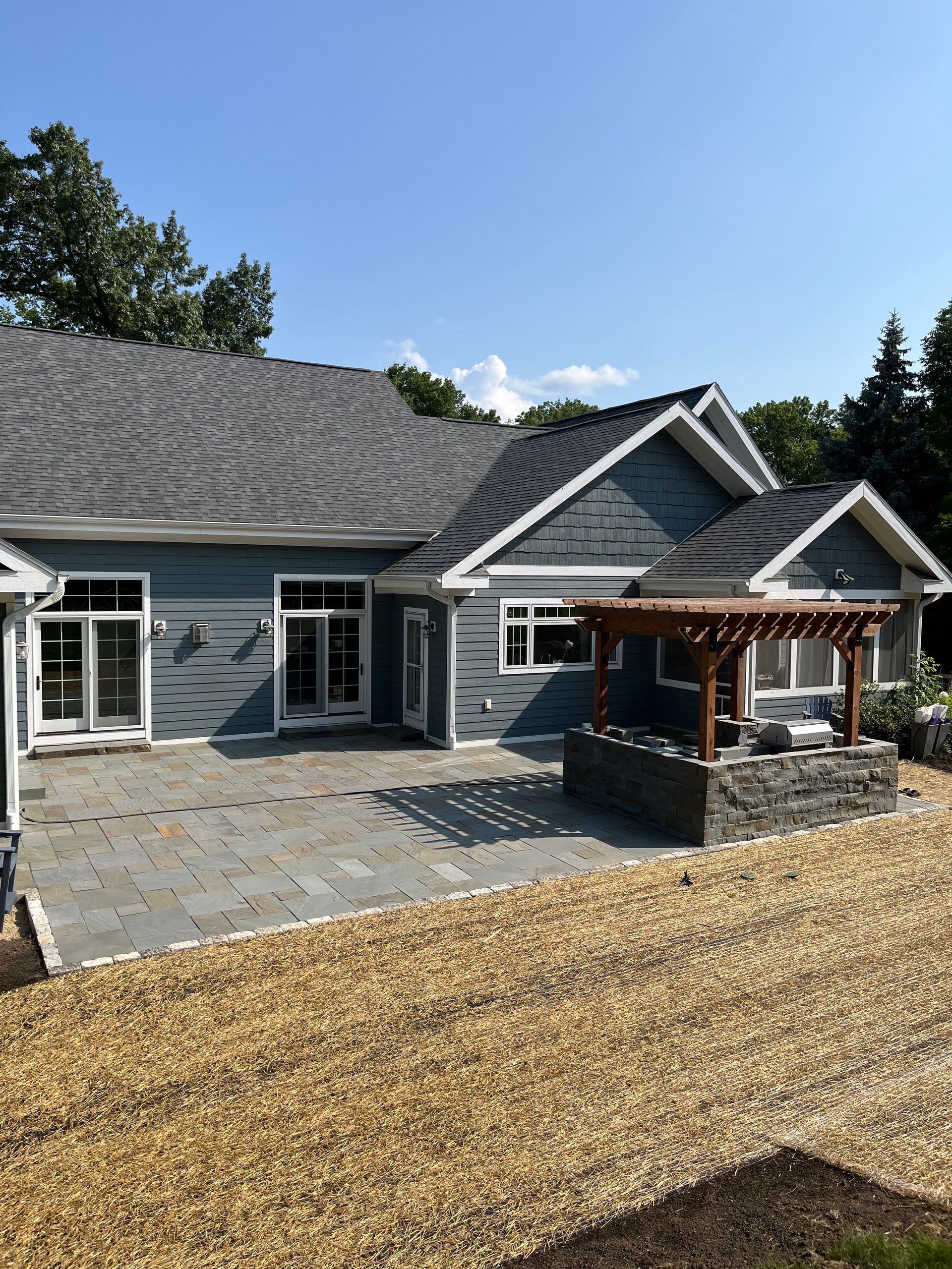 Stone retaining wall with steps, next to a red building with a black garage door, set in a gravel area and wooded hillside.
