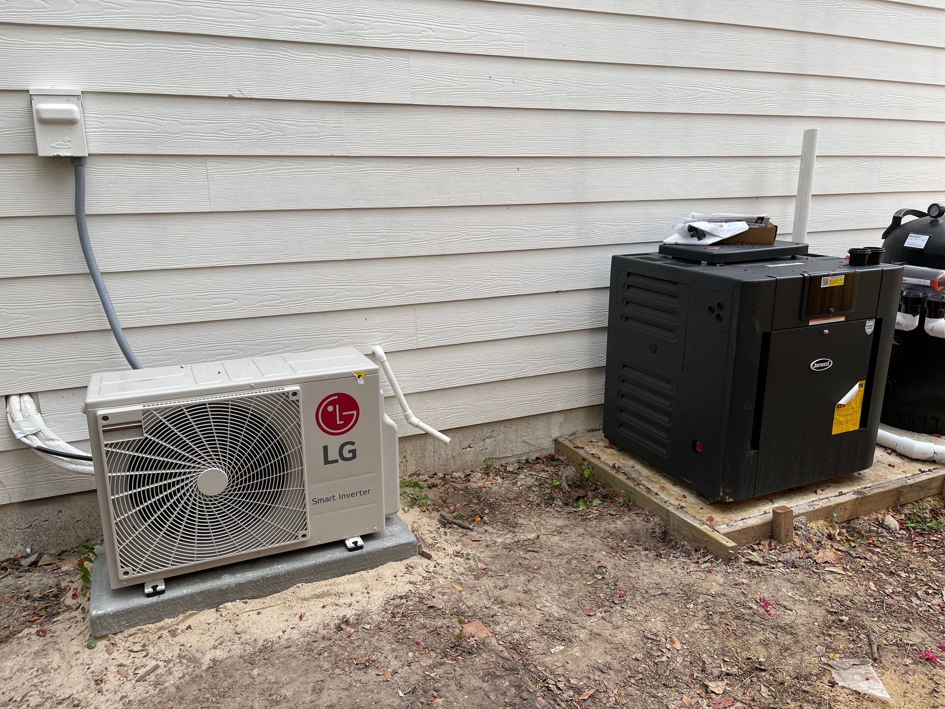 LG heat pump and black spa heater on concrete pads next to a light-colored house with siding.