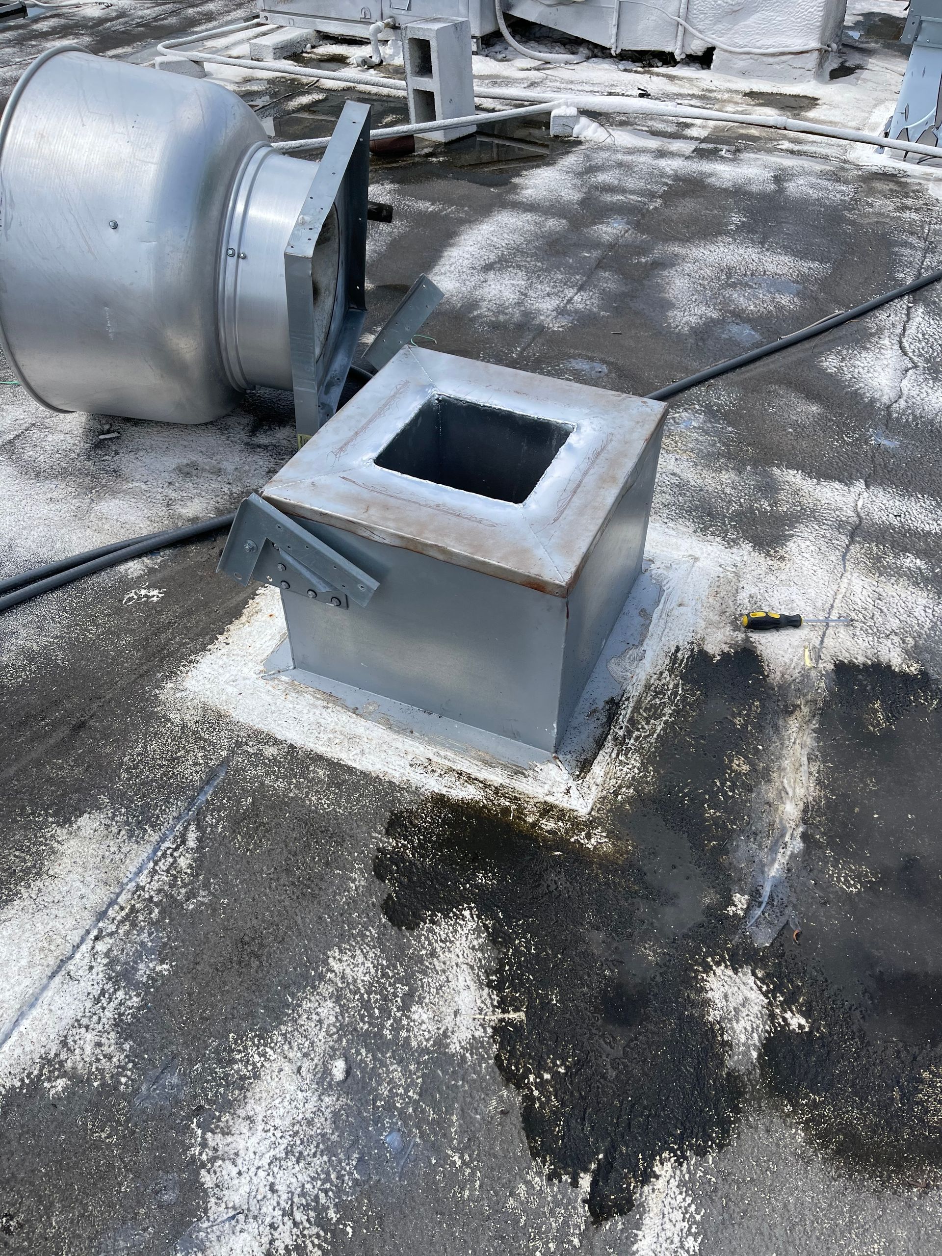 Metal roof vent parts scattered on a black tar surface, white sealant around a square vent.