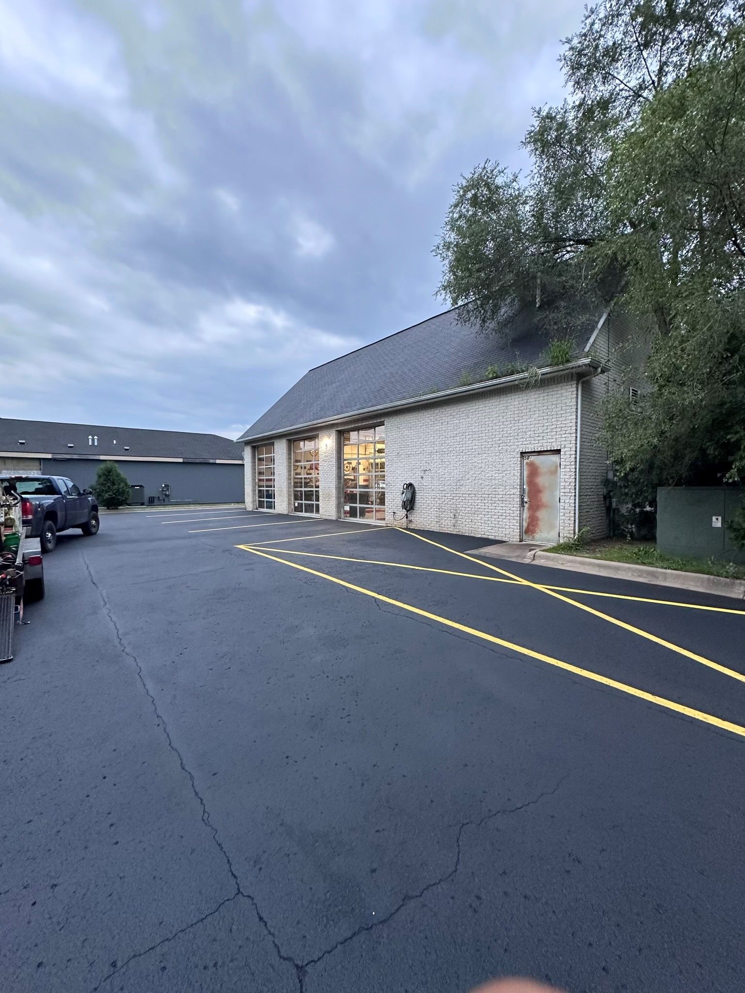 Asphalt parking lot in front of a light brick building with large glass windows and a dark roof.