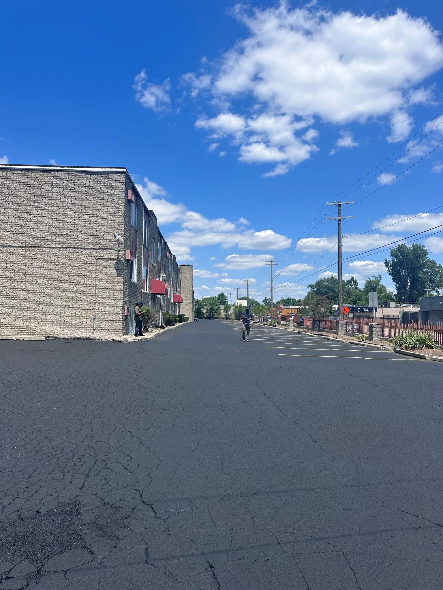 Paved street with building on the left and businesses on the right, under a bright blue sky with puffy clouds.