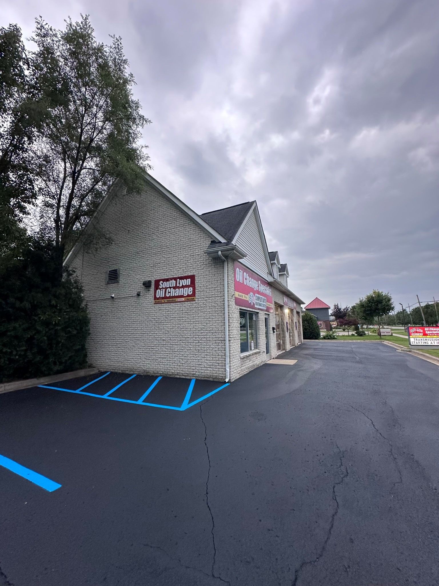 Exterior view of a small brick building with blue parking lines, cloudy sky, and a tree on the left.