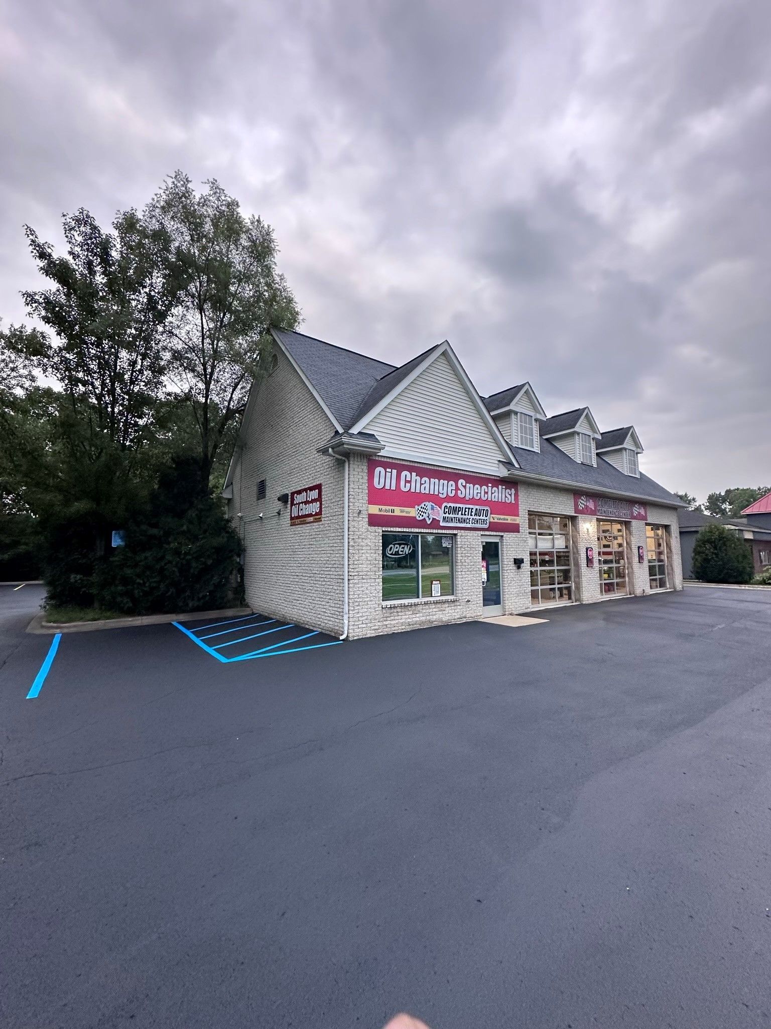 Building with business signage, light-colored brick exterior, and a dark-paved parking lot under an overcast sky.