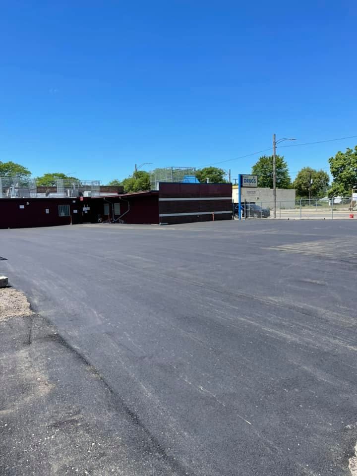 Paved parking lot in front of a dark building with a blue sky.