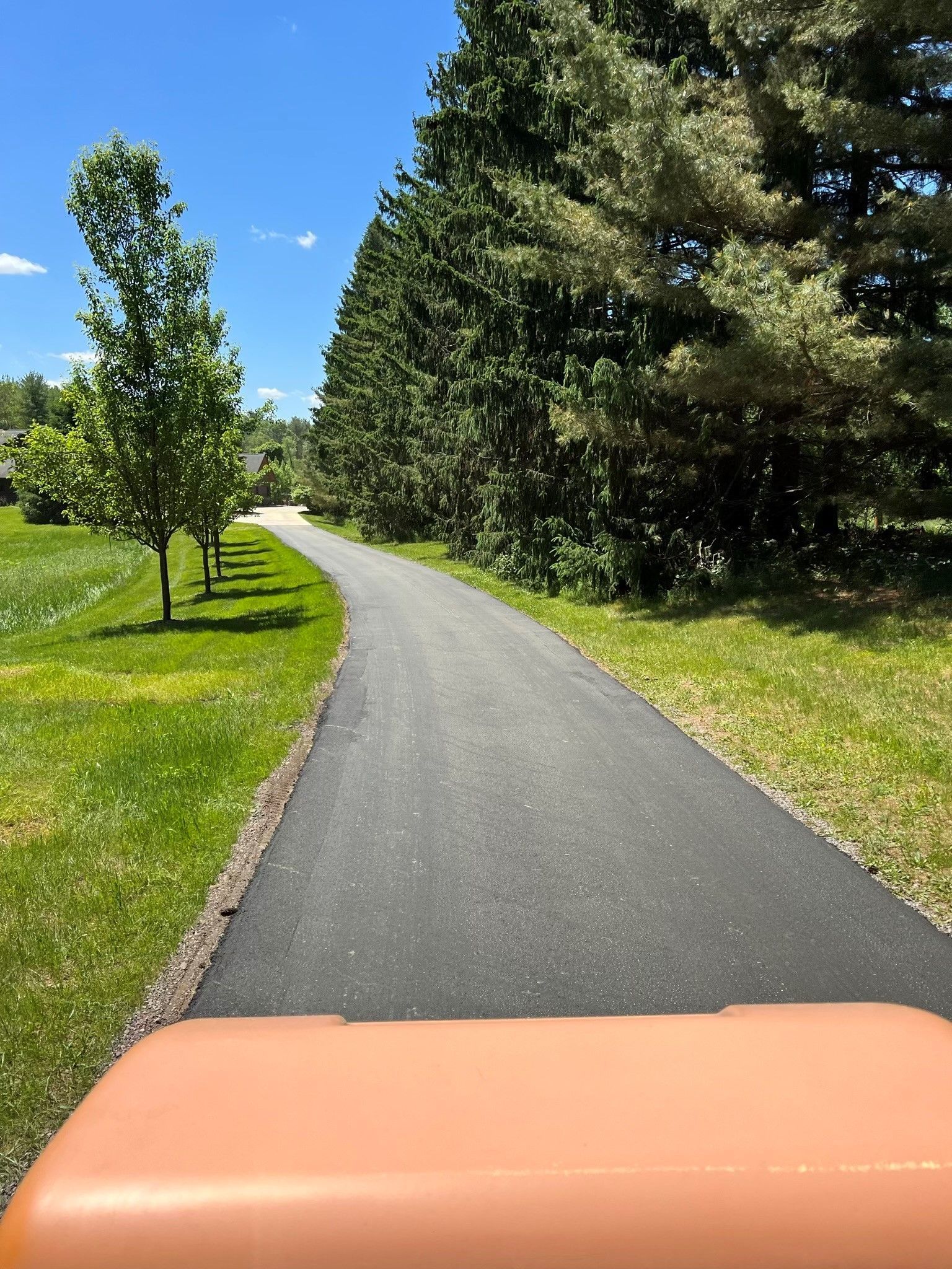 Paved path curves through green grass and trees, view from a vehicle's dashboard on a sunny day.