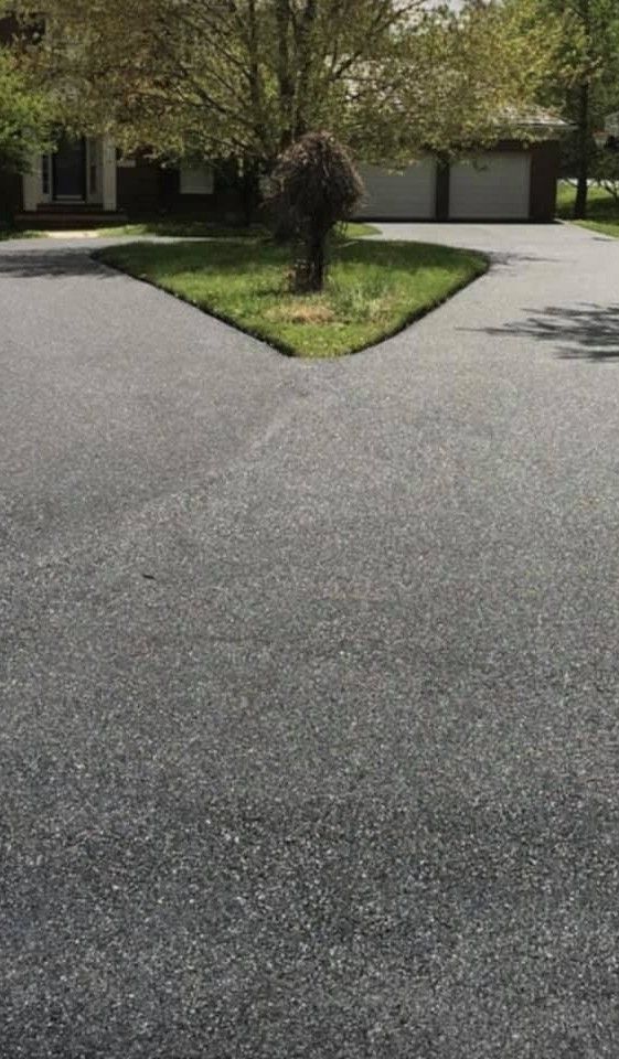 Asphalt driveway splitting into two directions around a small patch of grass with a bush.