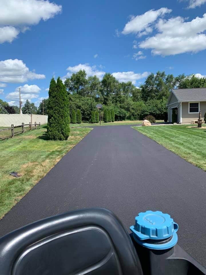 Newly paved driveway with green lawn, trees, and blue sky. View from a riding mower.