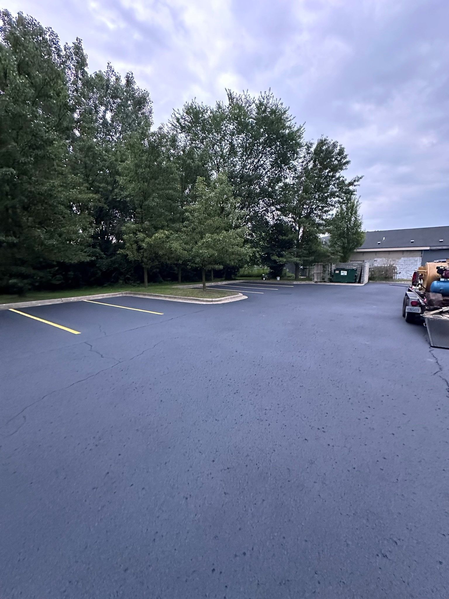 Paved parking area with trees in the background under a cloudy sky.