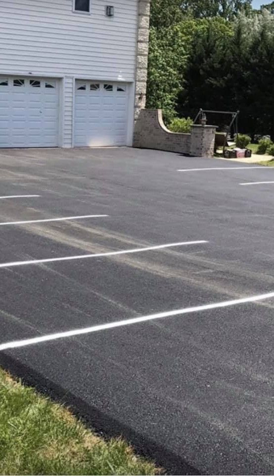Asphalt driveway with white parking lines, two garage doors, and a stone wall.