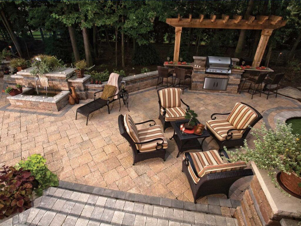 Patio with wicker chairs around a fire pit, outdoor grill, and stone seating area surrounded by greenery