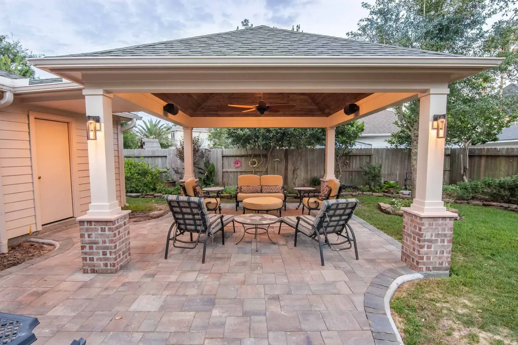 Covered backyard patio with stone pavers, outdoor table and chairs, and a built-in grill area