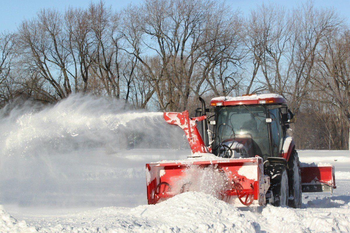 Red snowplow clearing a snowy road, spraying snow with bare trees in the background