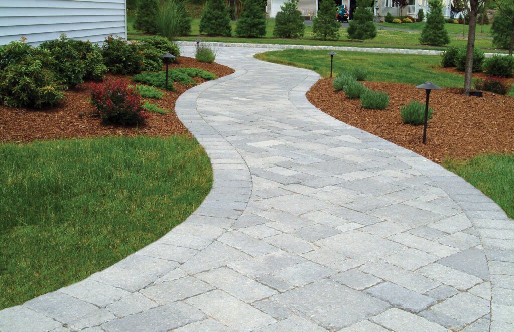 Curving light-gray stone walkway through a landscaped garden with green grass and shrubs