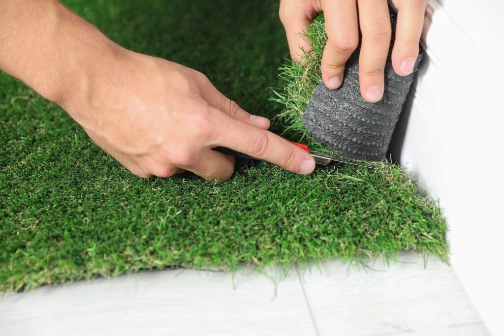Hands installing artificial grass on a white surface