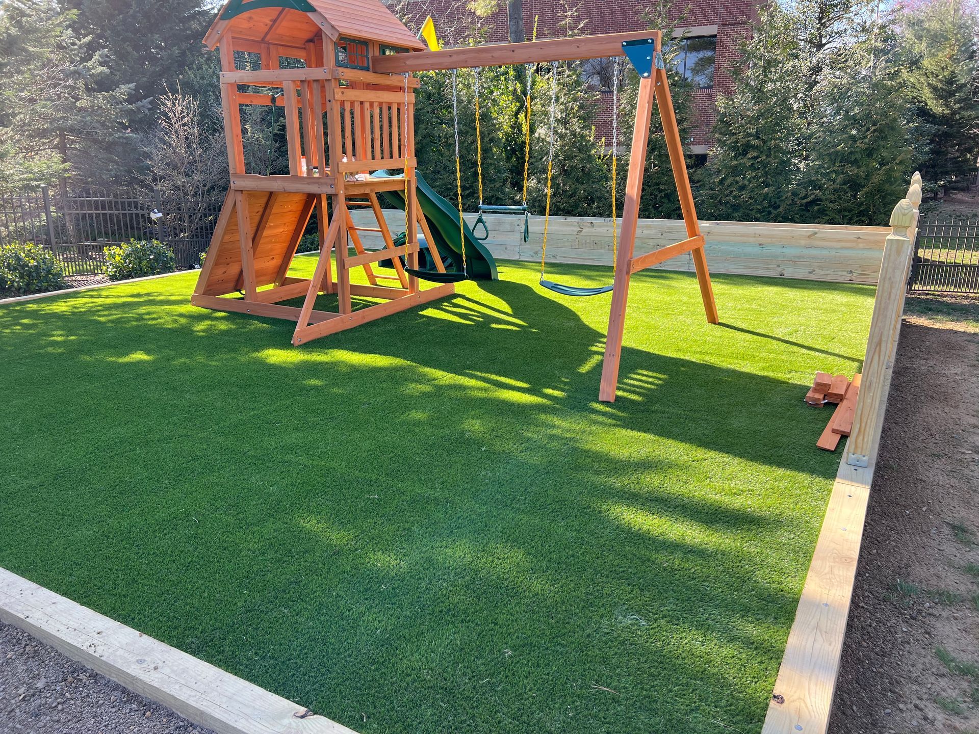 Backyard playground with wooden playset, swing, slide, and green artificial turf in bright sun