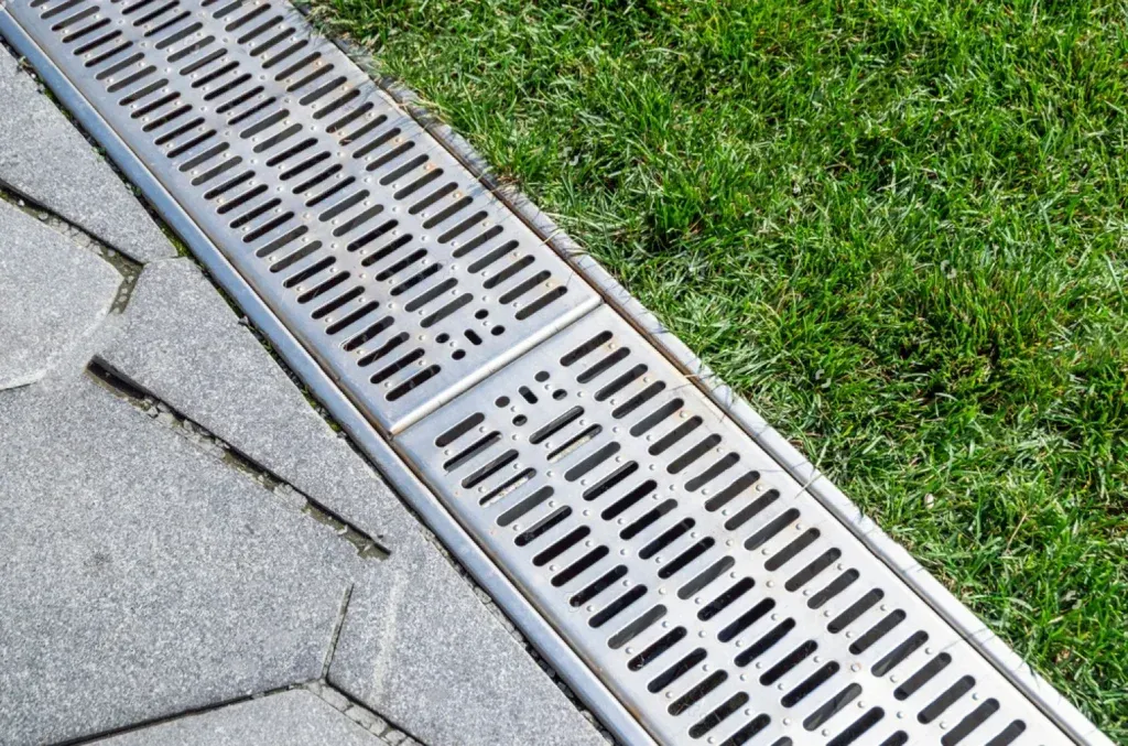 Roof drain grate beside gray shingles and green grass