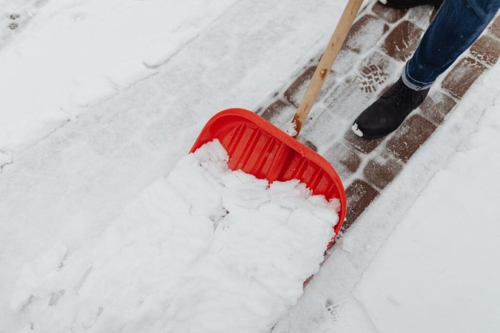 Person shoveling snow with a red snow shovel on a snowy walkway