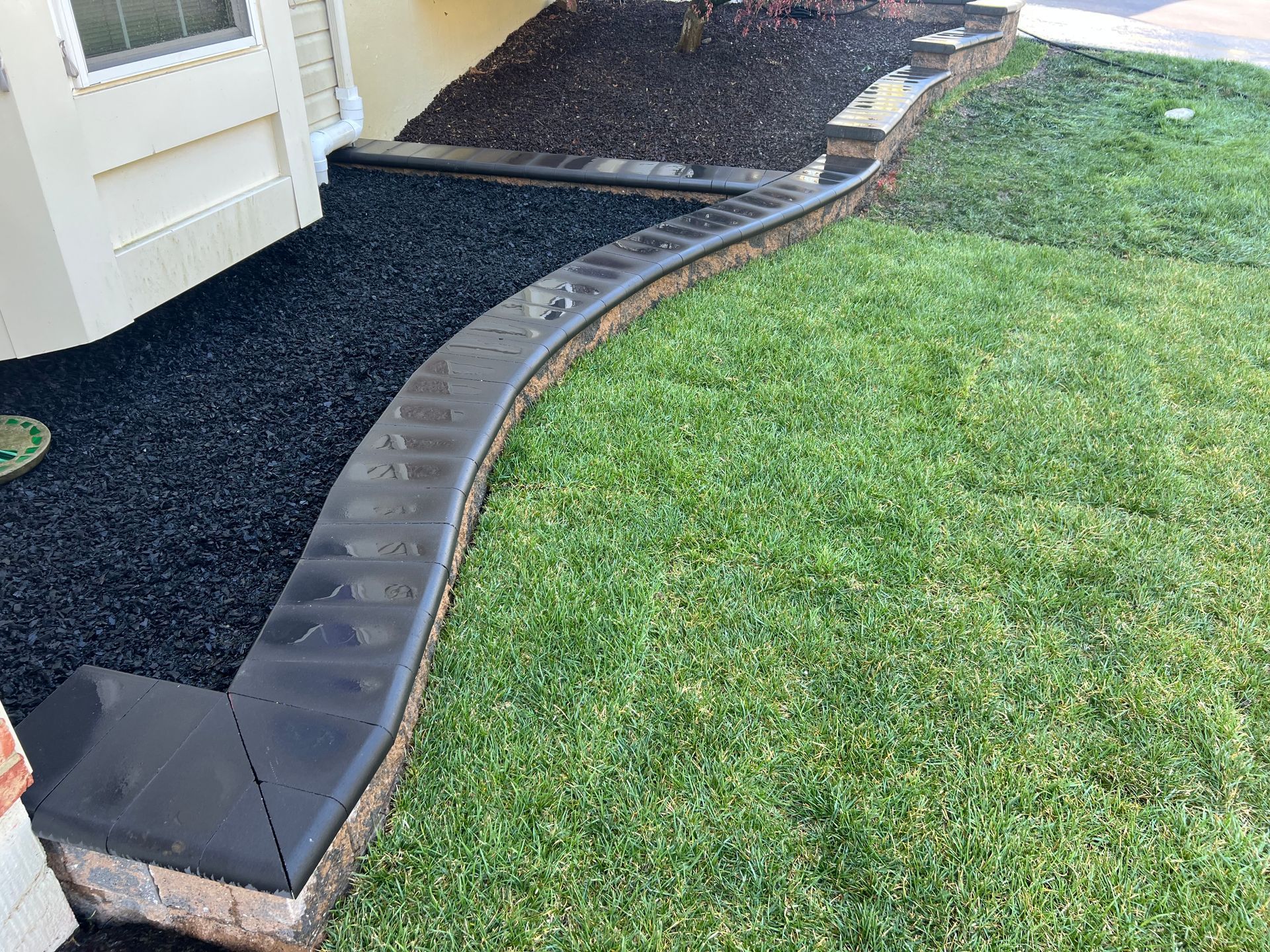 Curved black garden edging separating a grass lawn from a gravel path beside a house