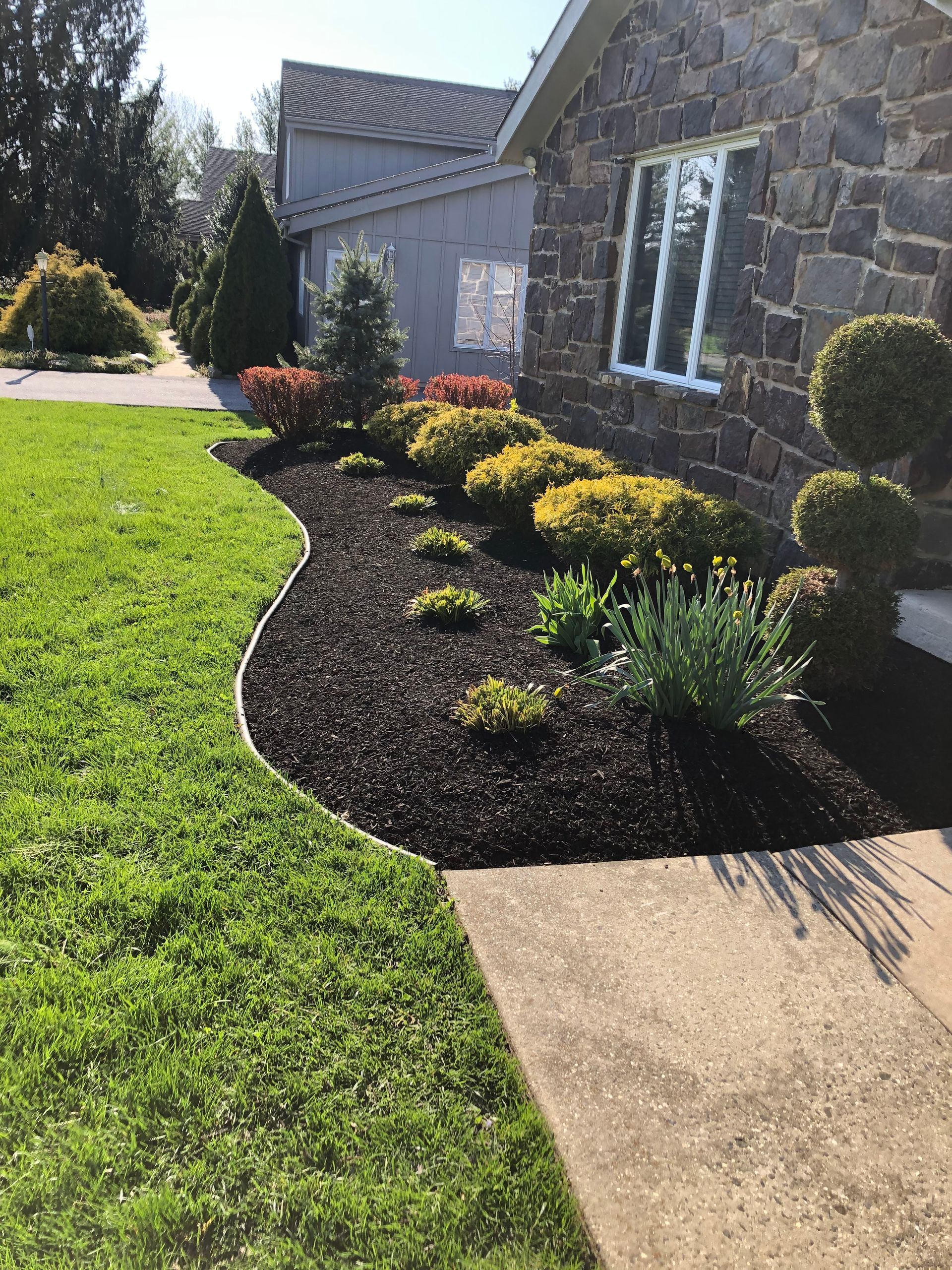 Landscaped front yard with green lawn, stone walkway, and flower bed beside a gray house.