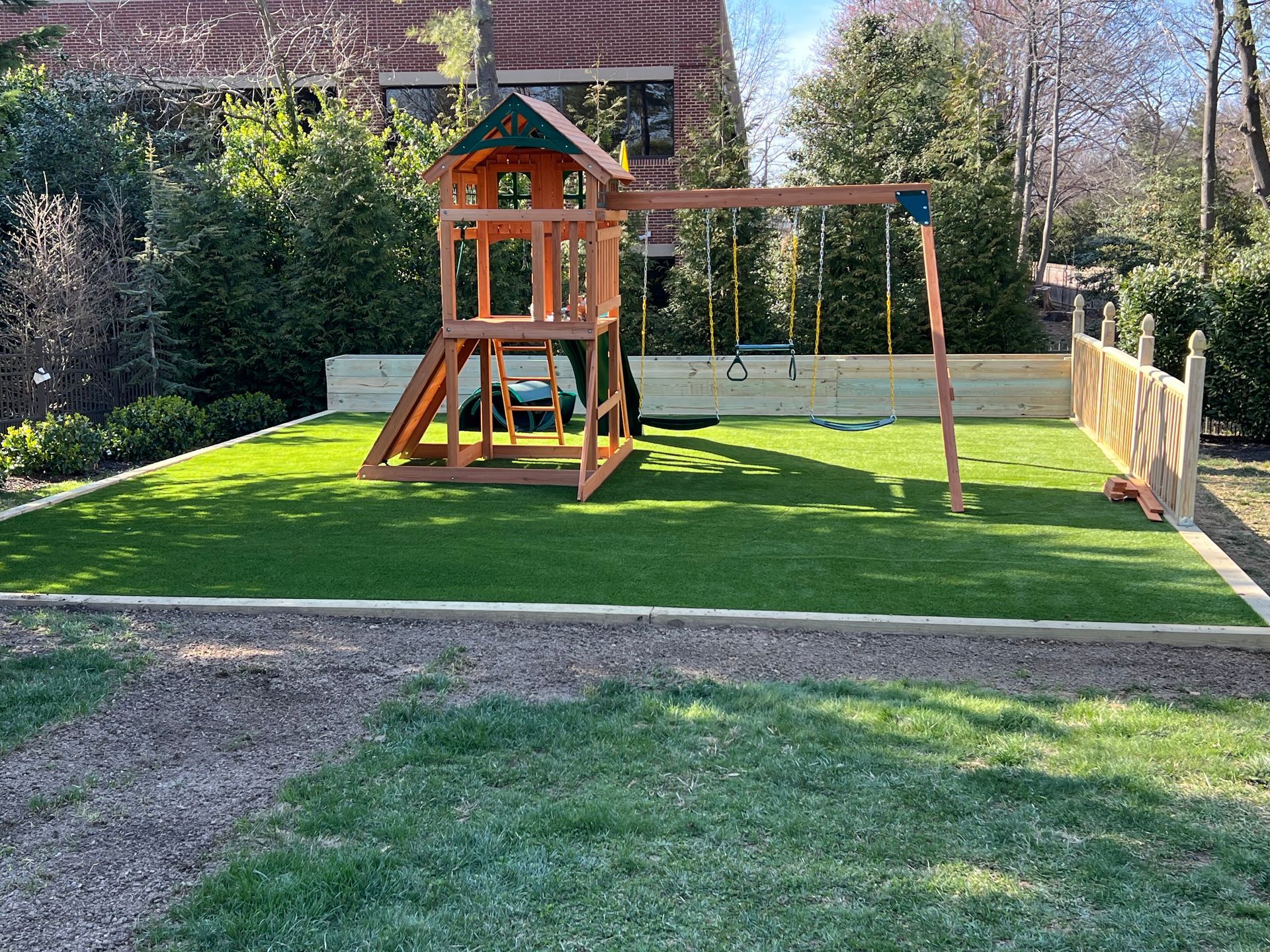 Backyard playground with a wooden playset, swing, and green turf in a fenced yard